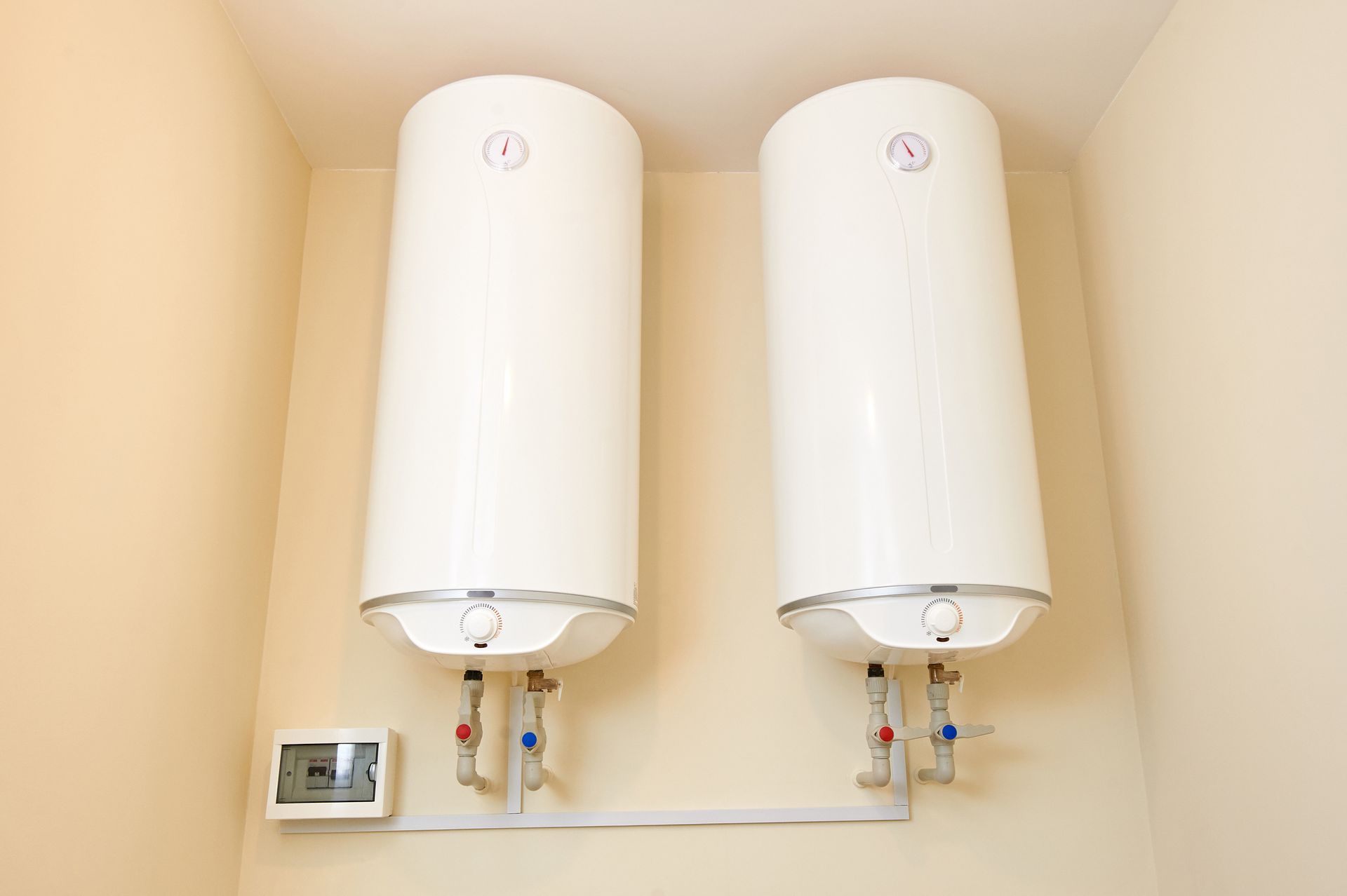 Two white wall-mounted electric water heaters with connecting pipes below