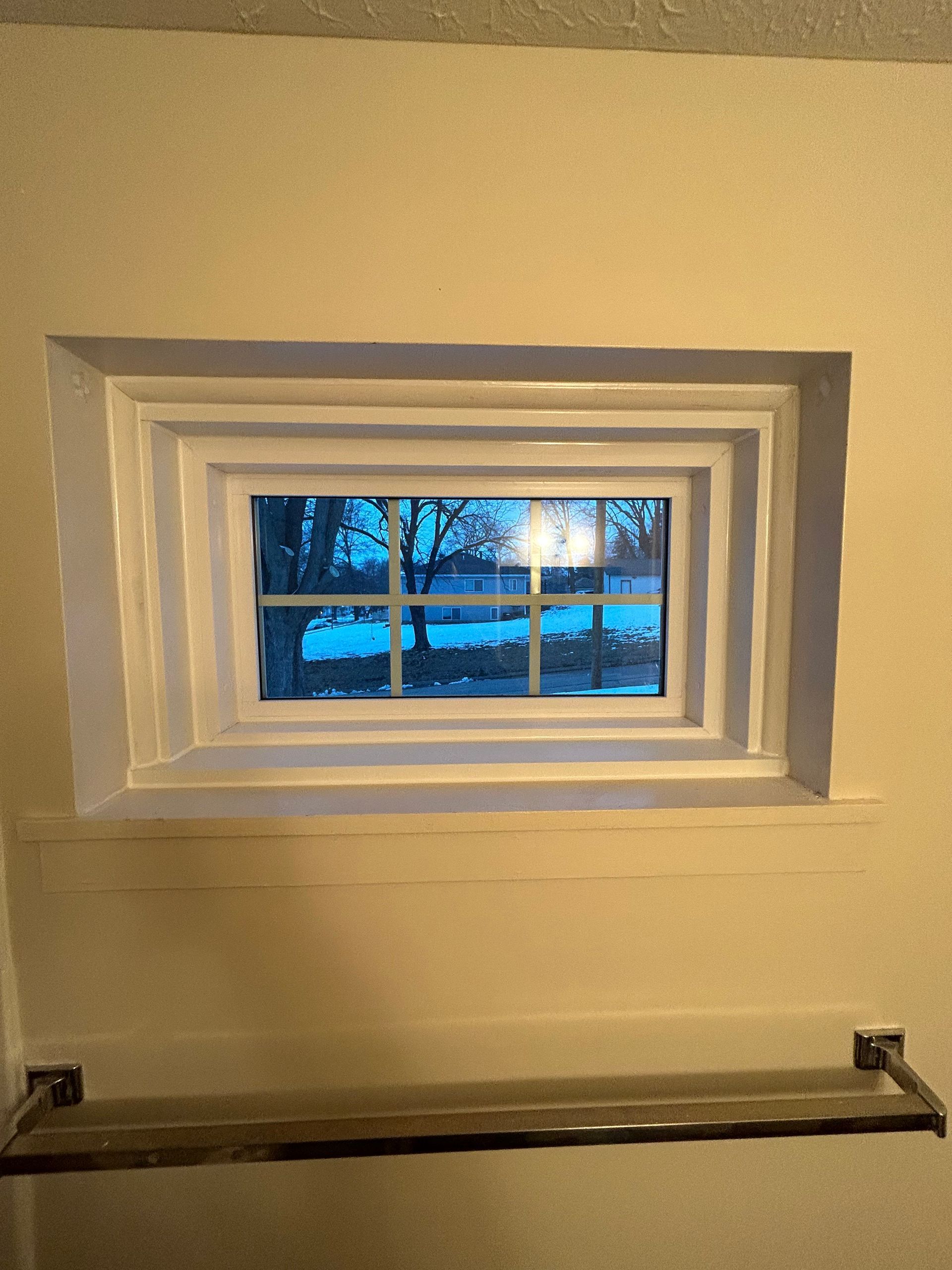 A bathroom window with a towel rack next to it.