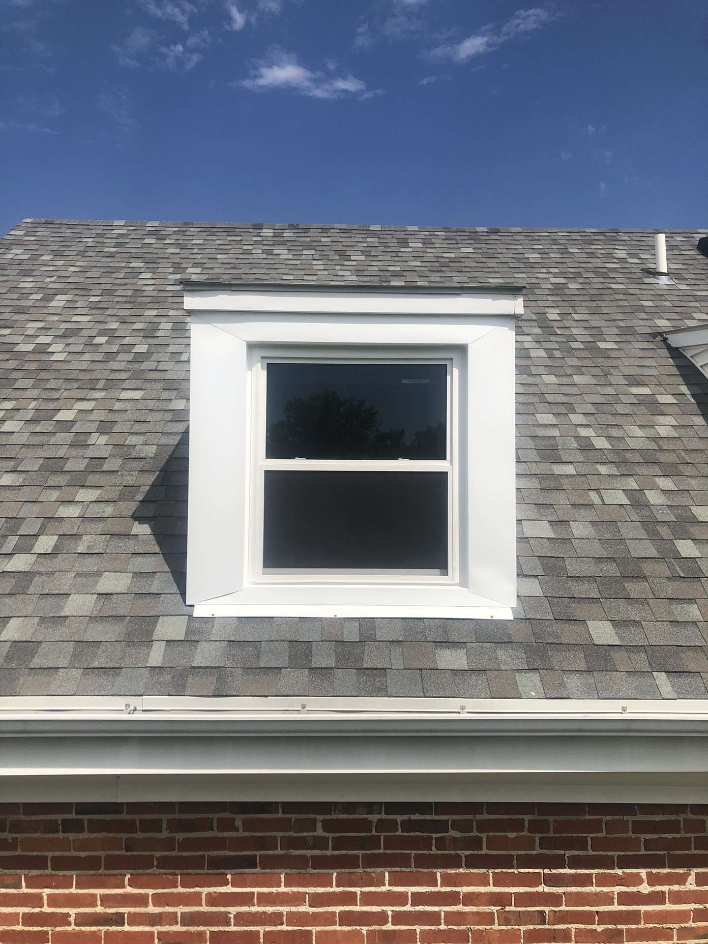 There is a window on the roof of a brick house.