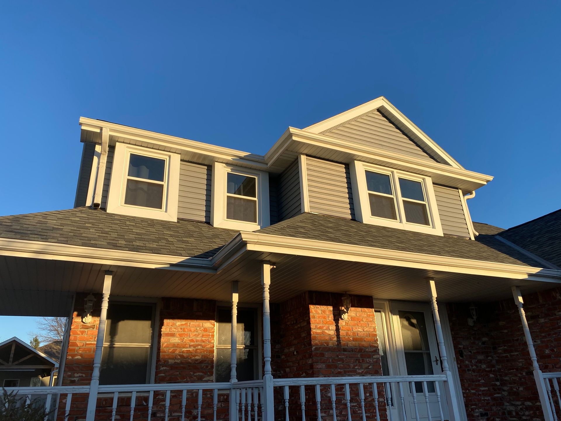 A brick house with a large porch and a gray roof.