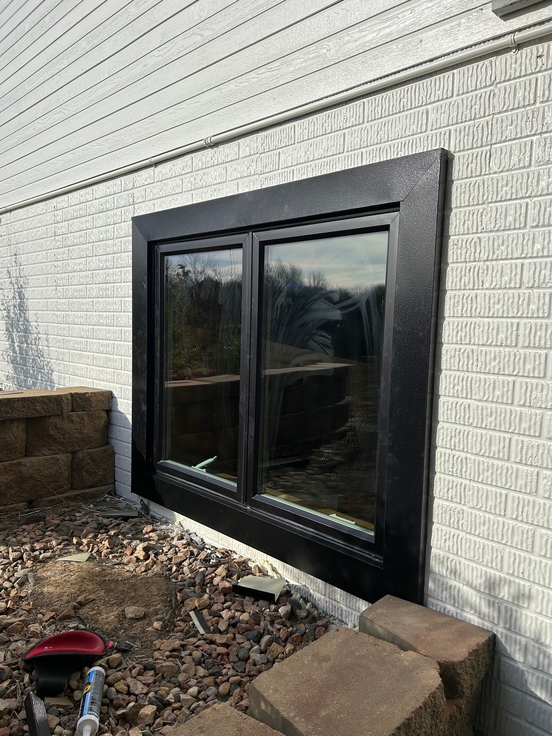 A window on the side of a white brick building with a black frame.