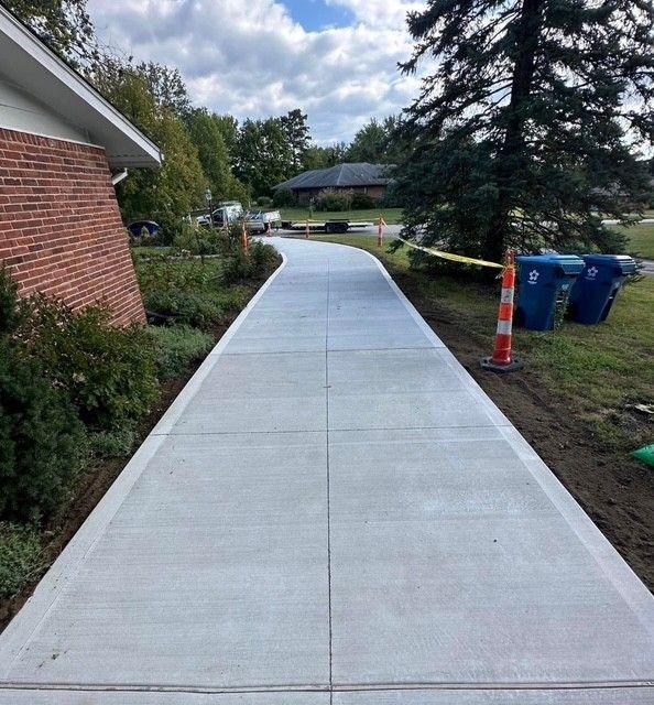 A concrete contractor with a yellow helmet is straightening and smoothing fresh driveway. A concrete contractor with a yellow helmet is straightening and smoothing fresh driveway.