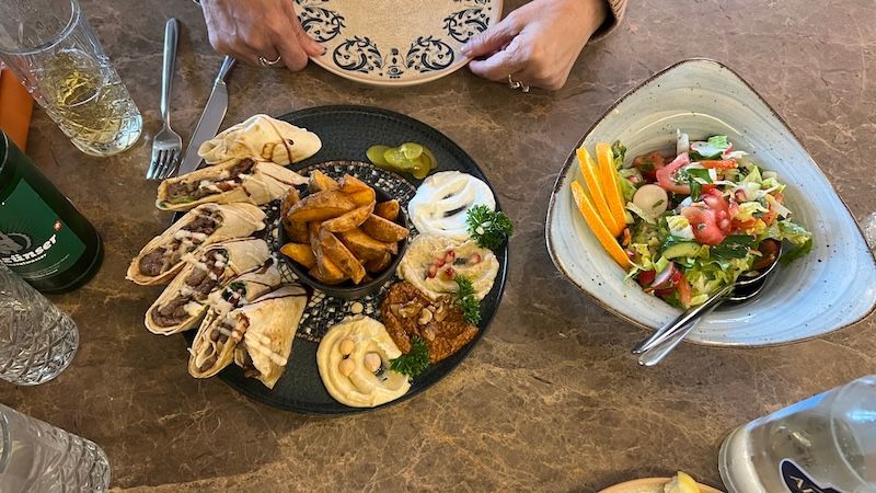 A restaurant table in Switzerland is set with wraps, potato wedges, dips, salad, and drinks. The meal adds context to what food costs can look like when deciding is Switzerland worth visiting.