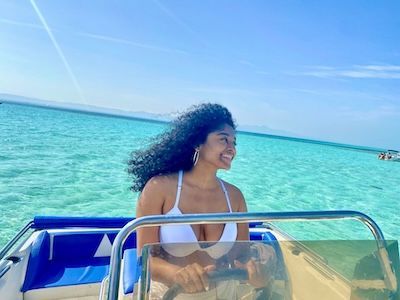 Jess smiles on a boat in a white swimsuit with bright turquoise water and a blue sky behind her.