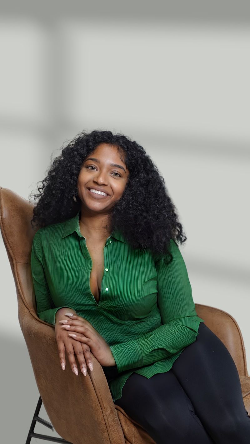 Jess, founder of She Found Wealth, smiling in a brown leather chair against a soft gray background.