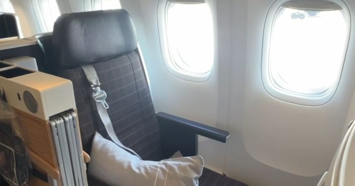 Swiss Air business class window seat with a plaid fabric backrest. A pillow rests on the seat beside