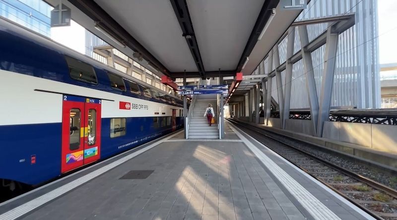 A double decker SBB train waits at a Swiss train station platform beside stairs and empty tracks. The clean station and easy rail access show why Switzerland is worth visiting without renting a car.