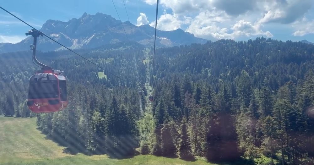Red cable car crossing a forest to Alpine mountains under a bright sky on scenic Switzerland trip. 