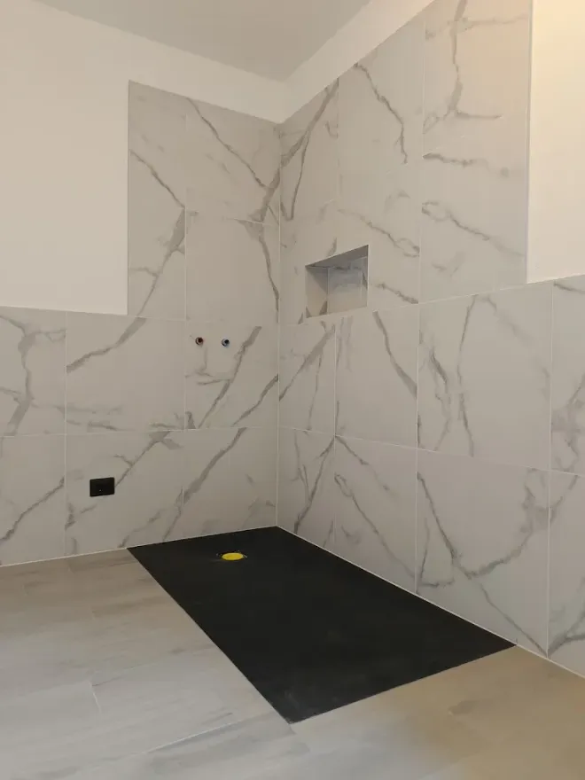 Confronto tra le ristrutturazioni del bagno: prima (vecchie piastrelle a fantasia) e dopo (moderne piastrelle bianche).