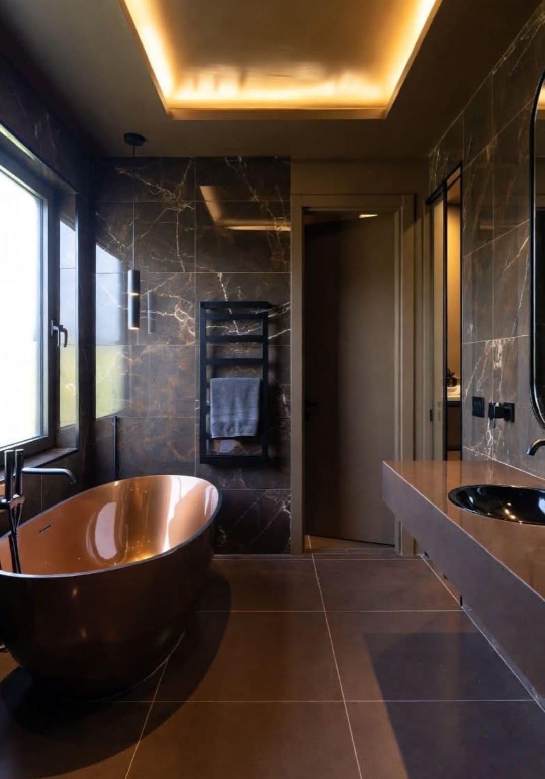 Bagno moderno con vasca in rame, pareti piastrellate scure e un soffitto caldo e illuminato.