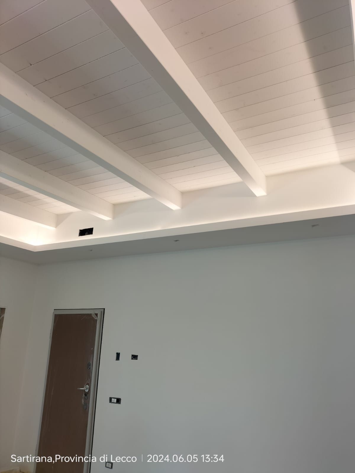 Soffitto bianco con travi in legno, illuminazione da incasso e pareti bianche.