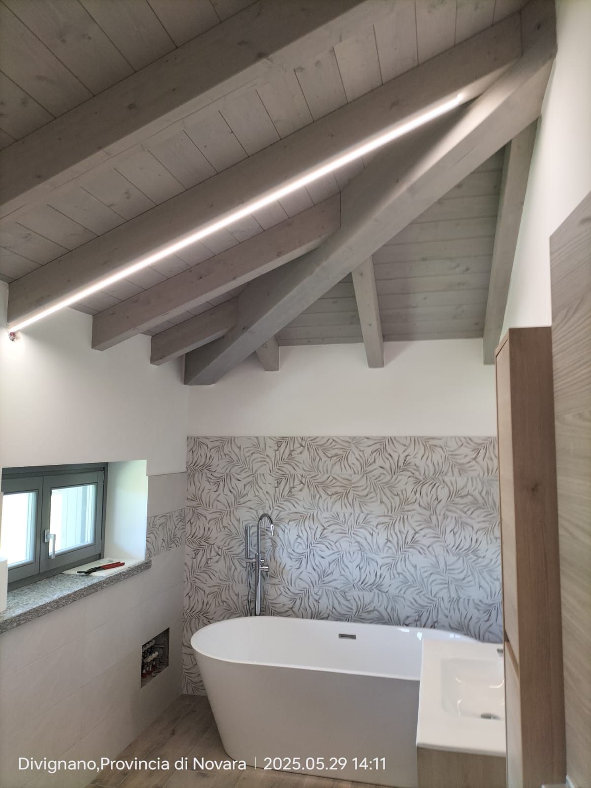 Bagno con vasca bianca indipendente, travi in legno e finestra.