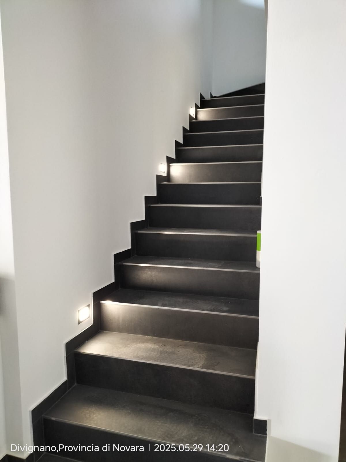 Scala grigio scuro con illuminazione da incasso, che sale contro pareti bianche.