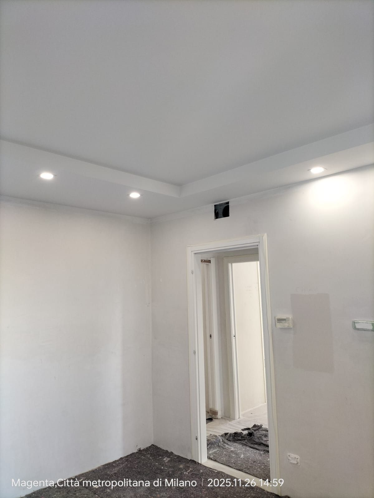 Interno di una stanza bianca appena dipinta, con luci incassate nel soffitto e una porta aperta.