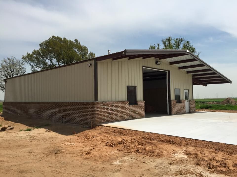 A large metal building with a brick wall is sitting in the middle of a dirt field.