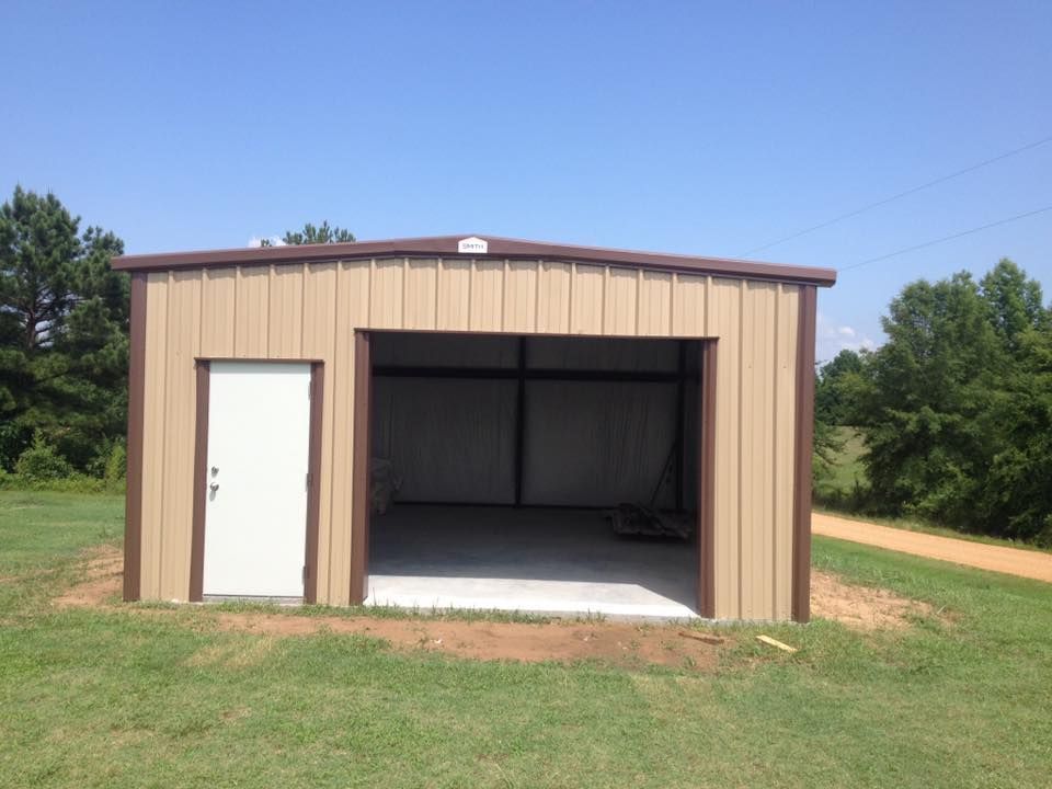 A brown metal garage with a white door is sitting in the middle of a grassy field.