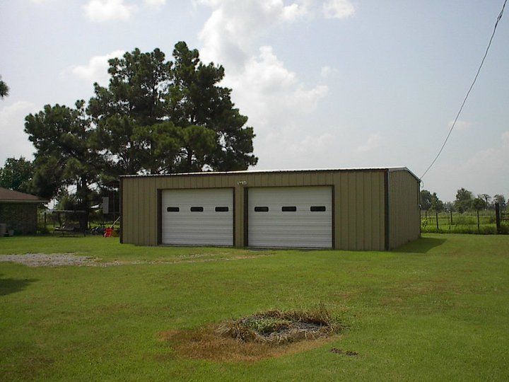 A garage with two white garage doors in a grassy field