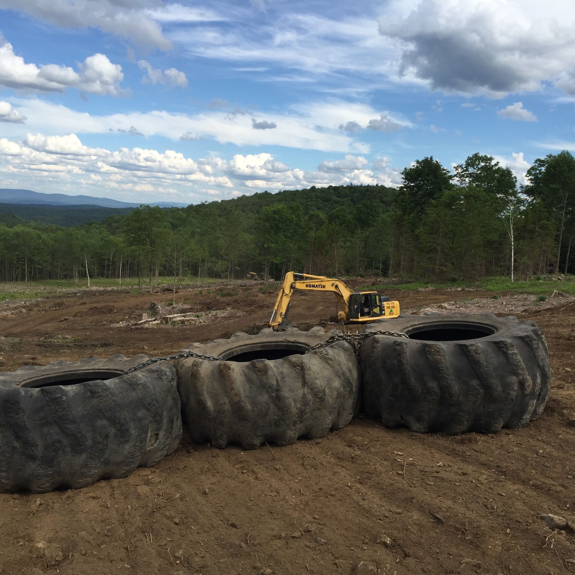 A yellow excavator is working in a field surrounded by tires