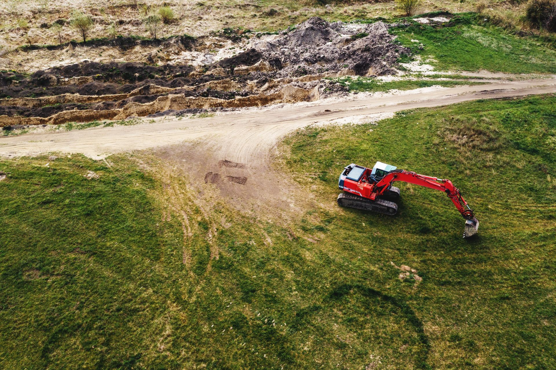 An aerial view of a red excavator digging in a grassy field.