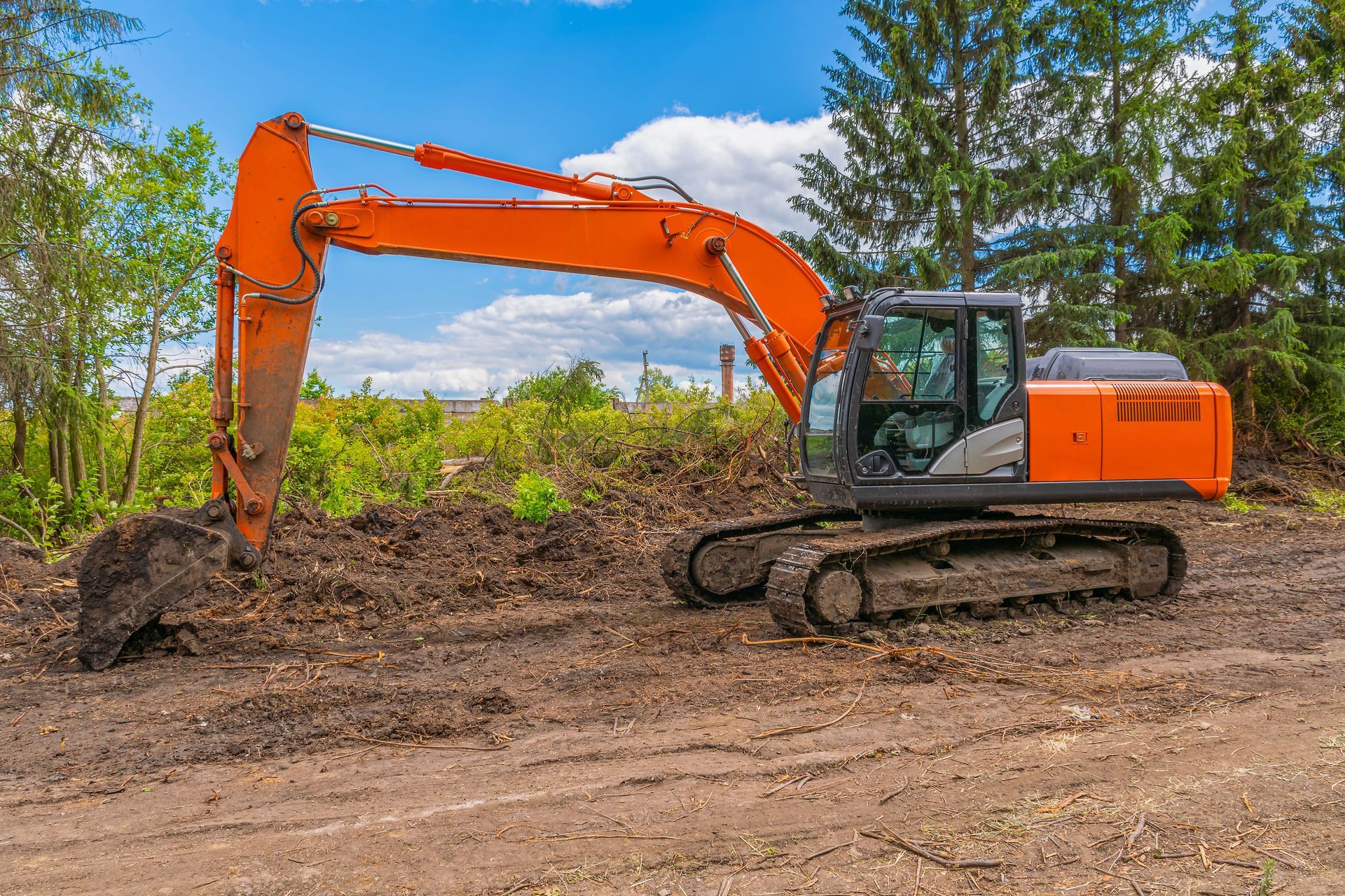 An orange excavator is digging a hole in a dirt field.