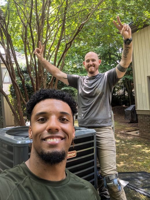 Two men are standing next to each other in front of an air conditioner.