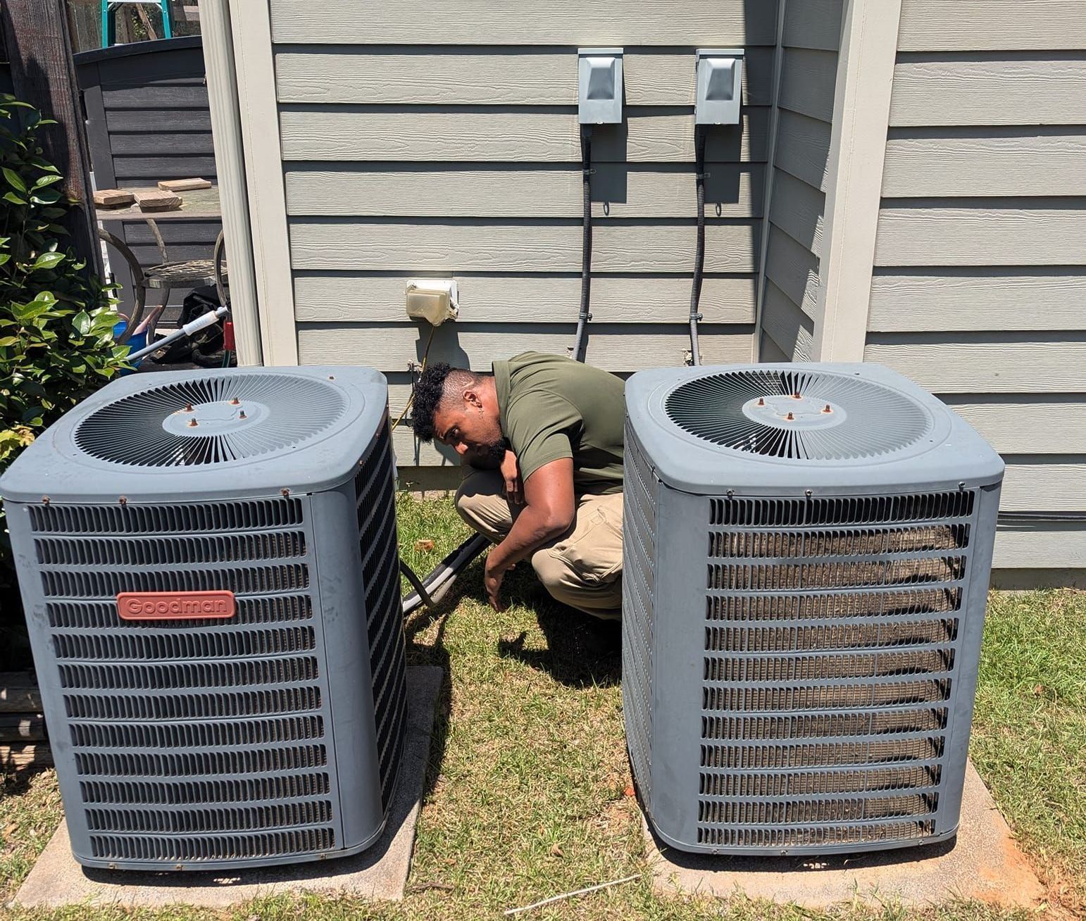 A man is working on two air conditioners in a backyard - Clayton, NC – Parker and Co Heating and Air, LLC