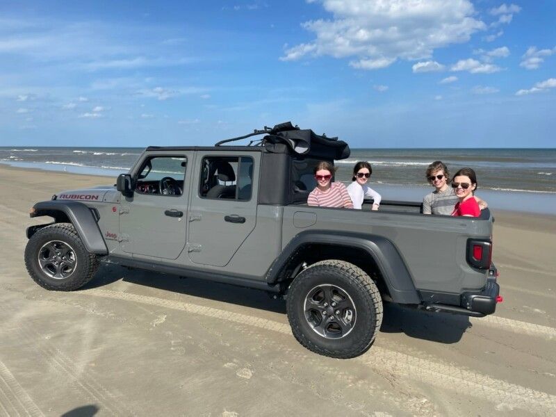 Silver Jeep Wrangler parked on a wet sandy beach near the ocean.
