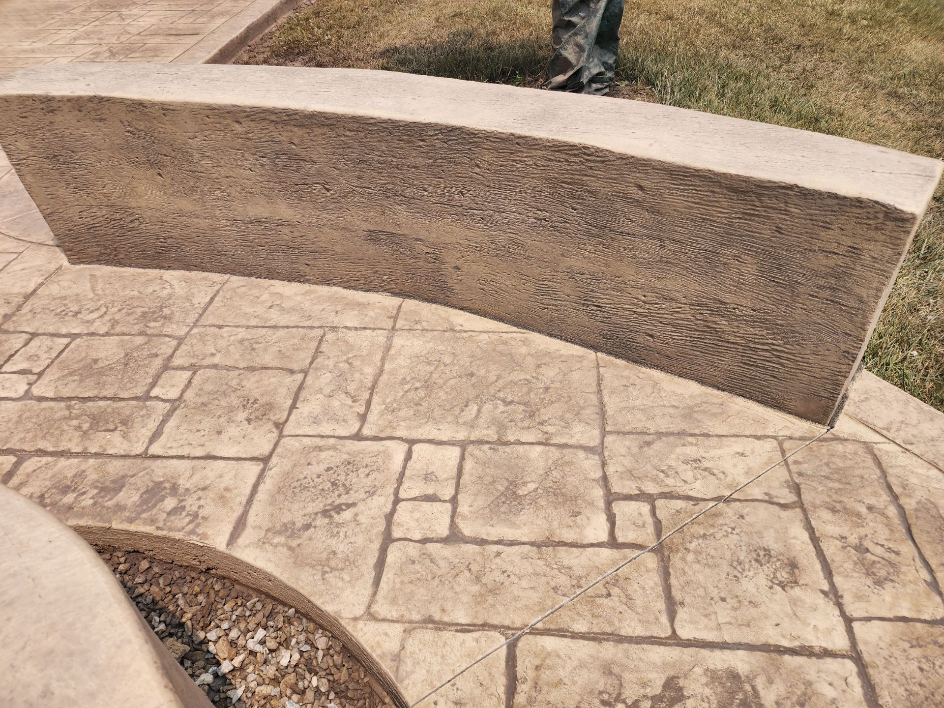 A person is standing next to a curved stone wall on a patio.