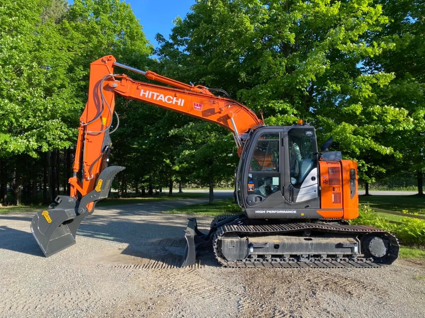 Une excavatrice Hitachi est garée sur une route de gravier dans un parc.