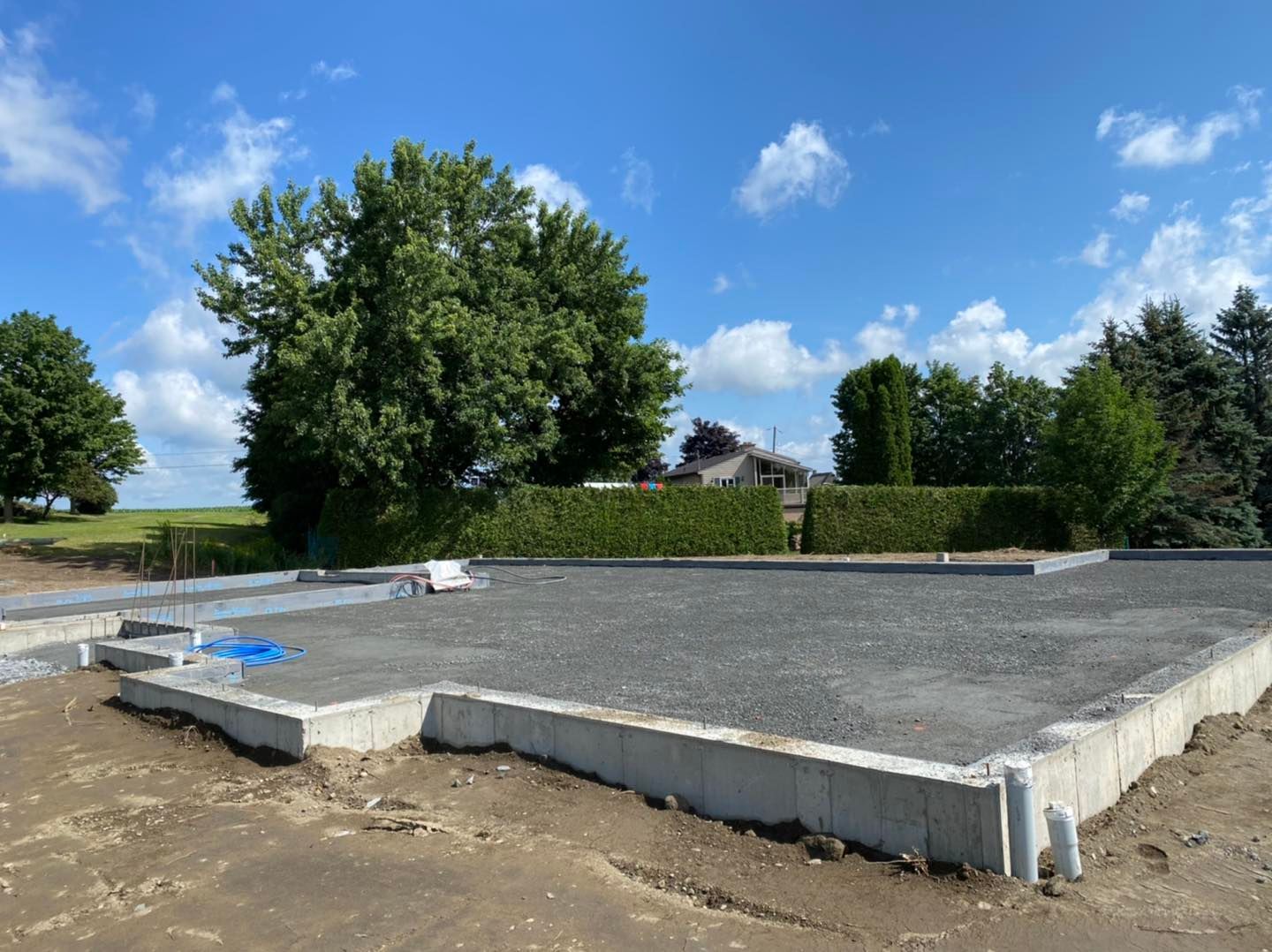 Une base en béton pour une maison est en cours de construction dans un champ avec des arbres en arrière-plan.