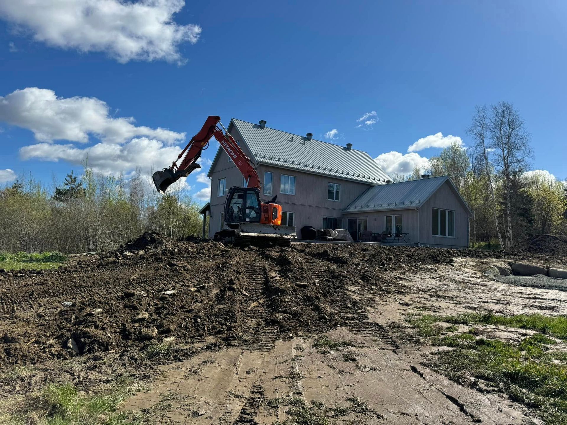 Une excavatrice creuse un trou devant une maison.