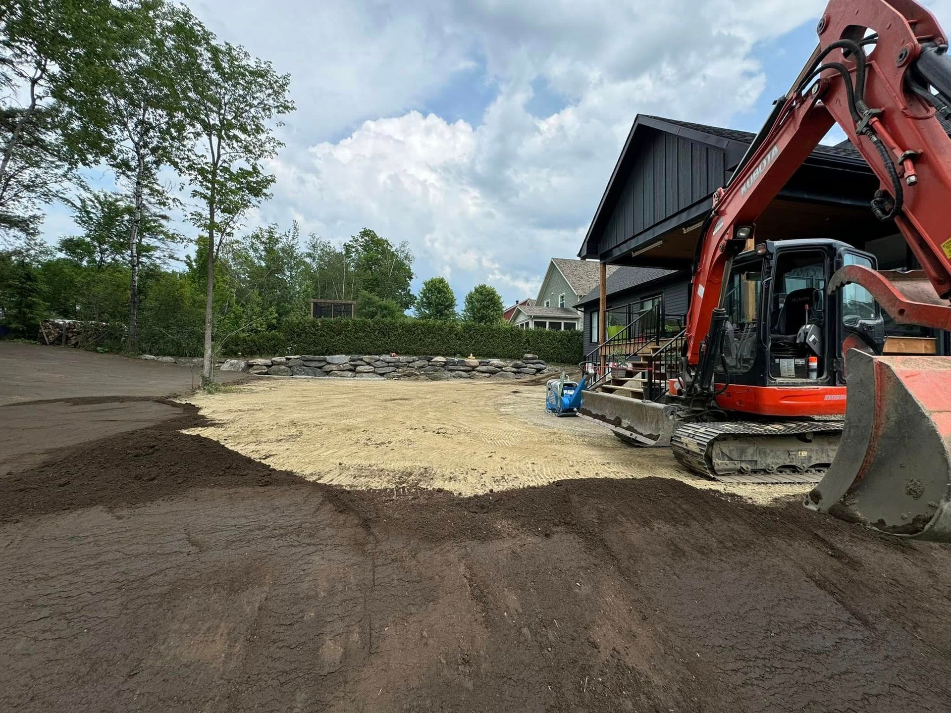 Une excavatrice déplace de la terre devant une maison.