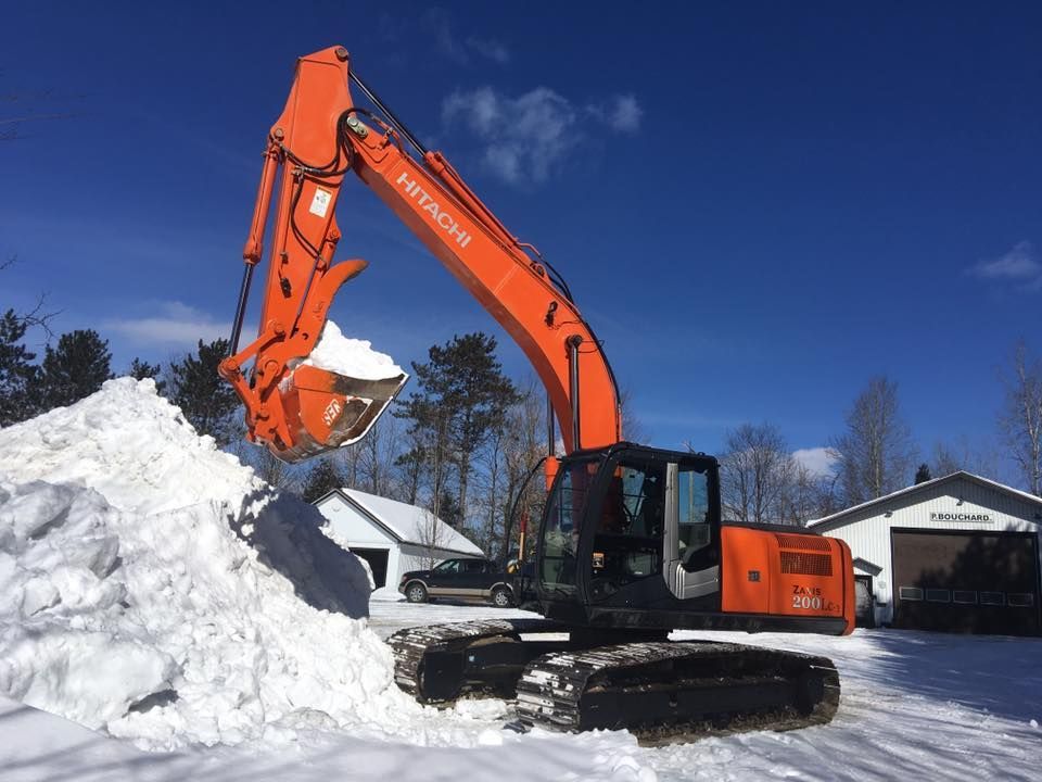 Une grande excavatrice orange ramasse la neige d'un tas.