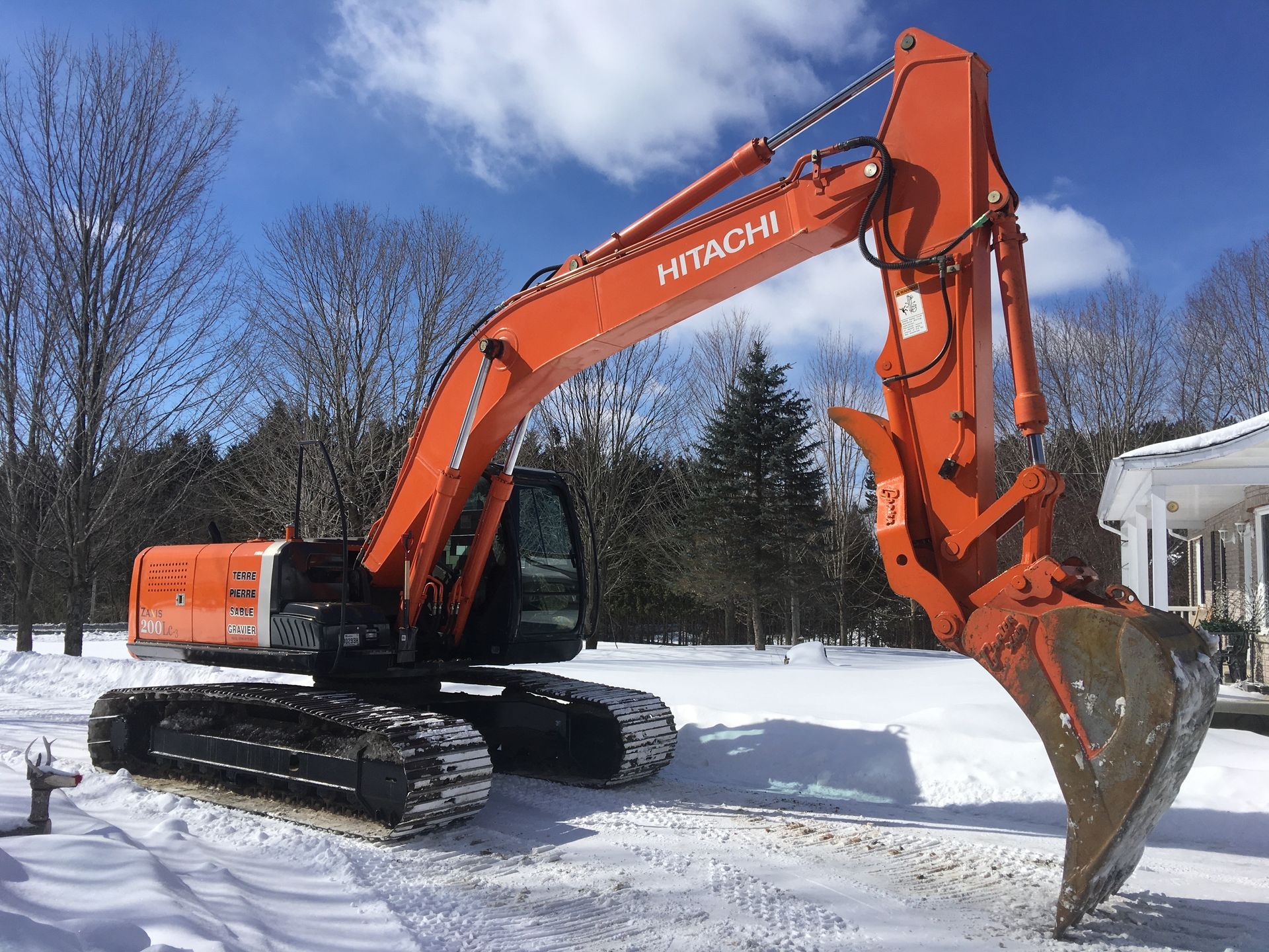 Une grosse excavatrice orange est garée dans la neige devant une maison.