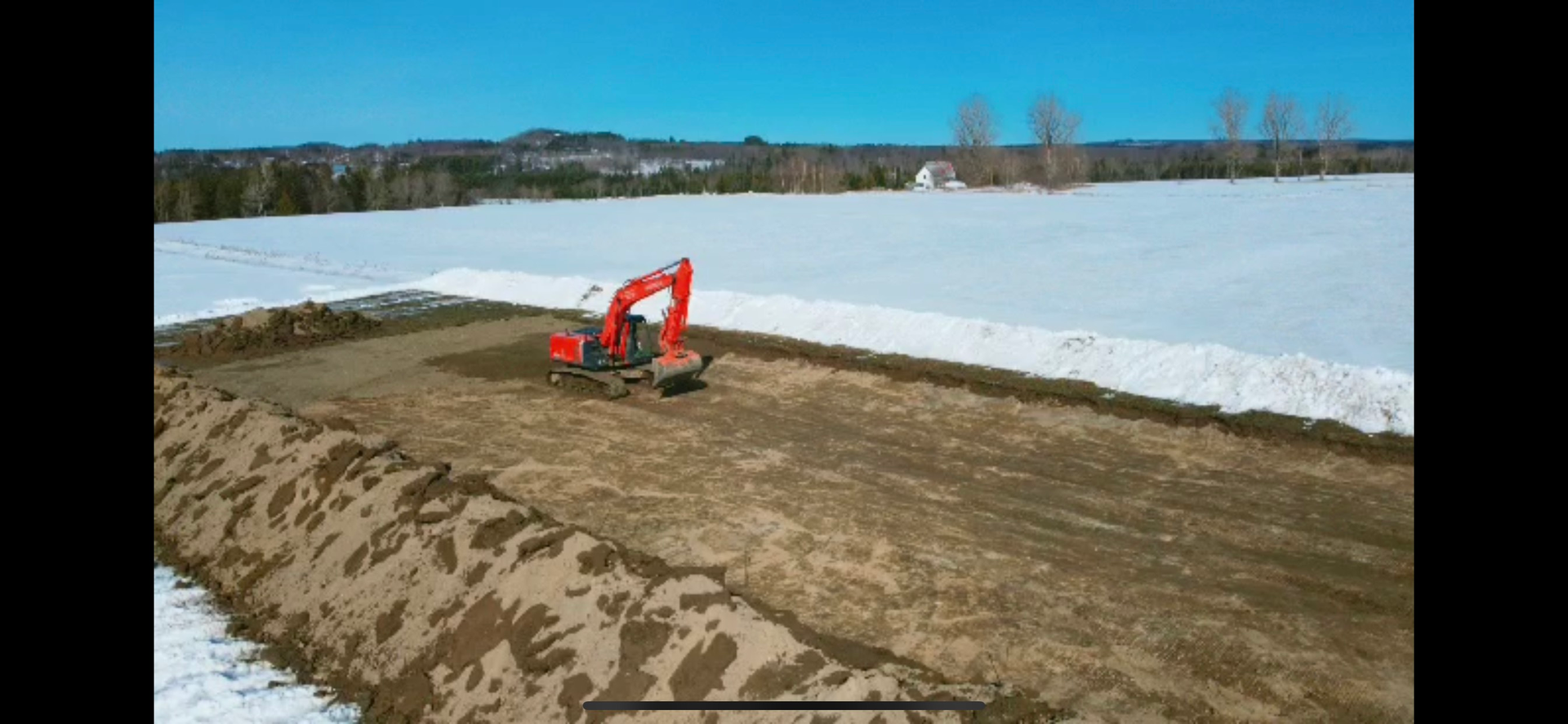 Une excavatrice rouge creuse un trou au milieu d'un champ enneigé.