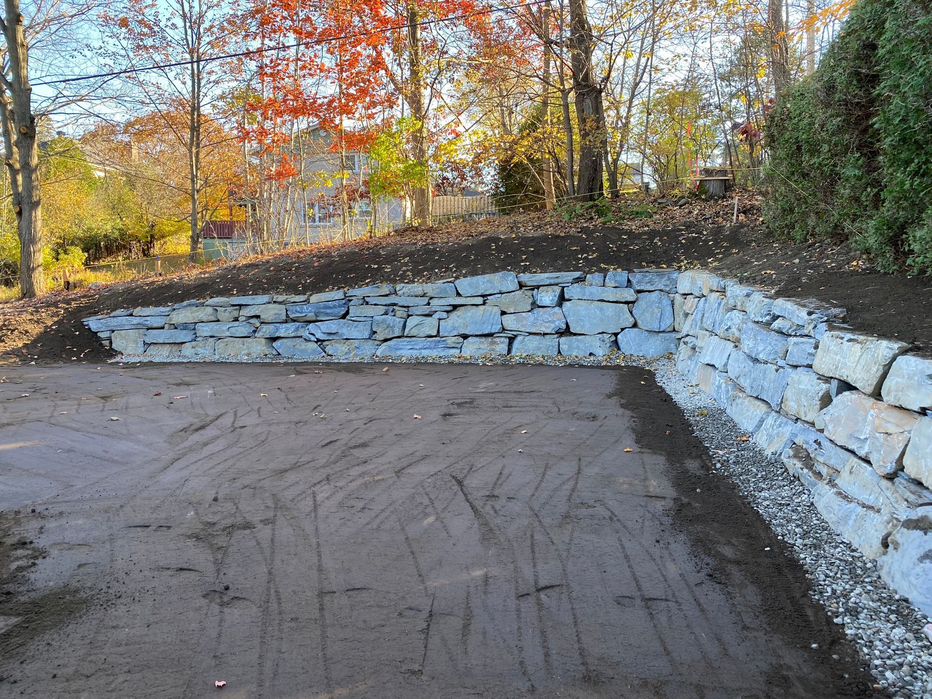 Un mur de pierre est en train d'être construit au milieu d'un chemin de terre.