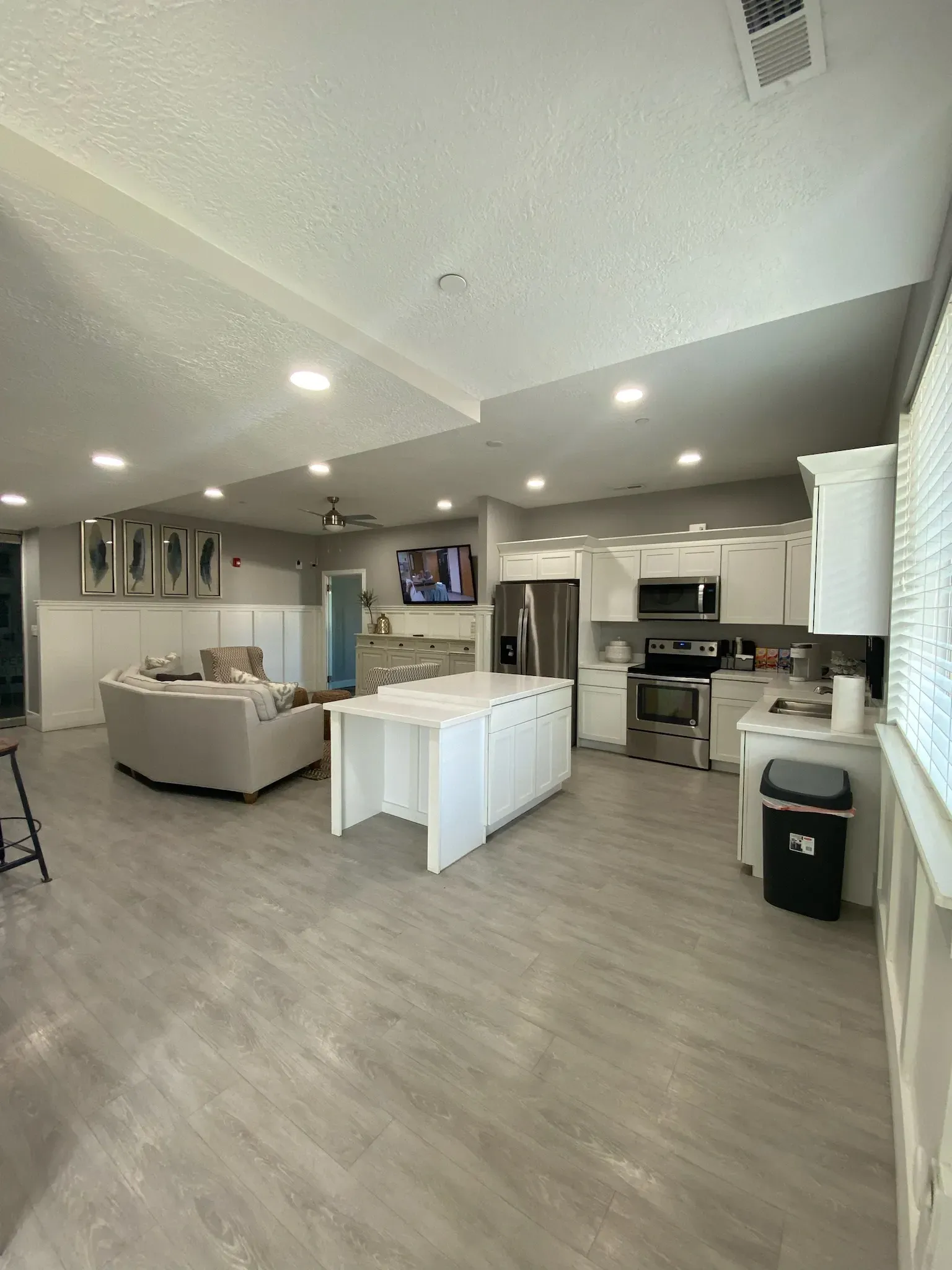 Bright open kitchen and living area with gray floors, white island, beige sofa, and recessed lighting