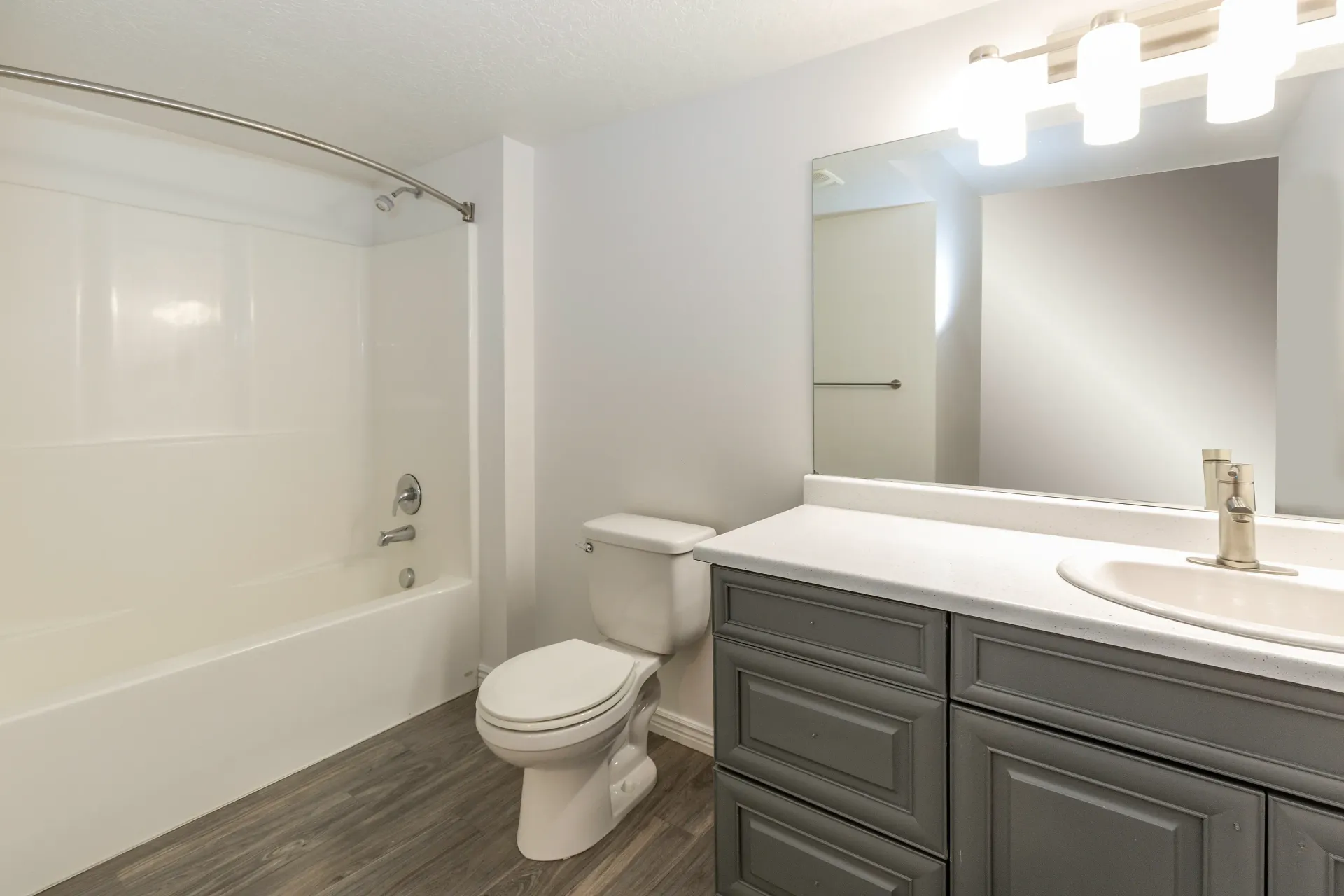 Bathroom with a white bathtub, toilet, and a gray vanity with a white countertop.