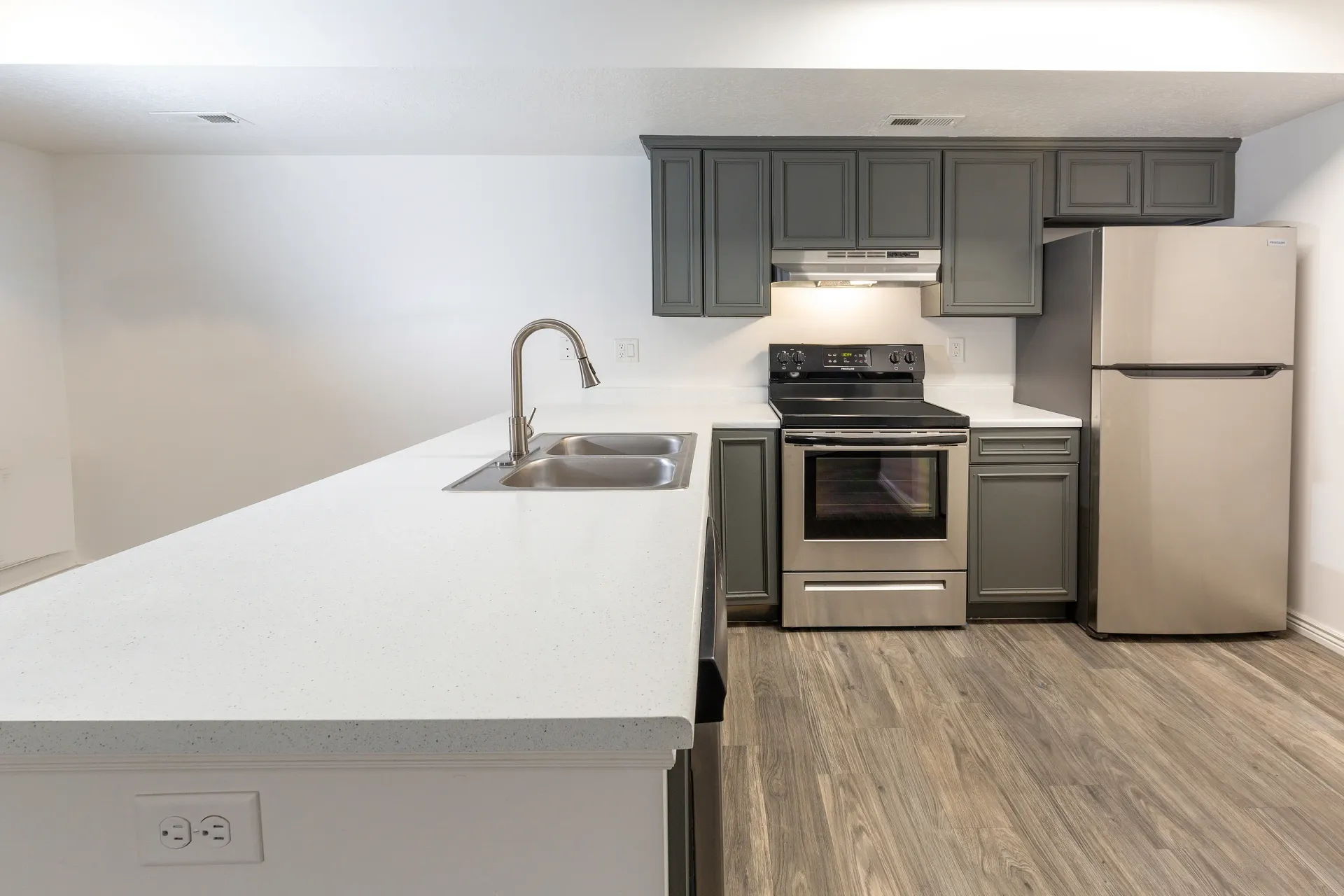 Modern kitchen with gray cabinets, stainless steel appliances, and a large white island with a sink.