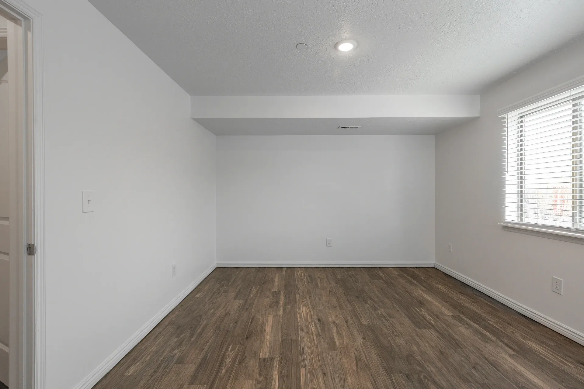 Interior of an empty room with white walls and wood-look flooring.