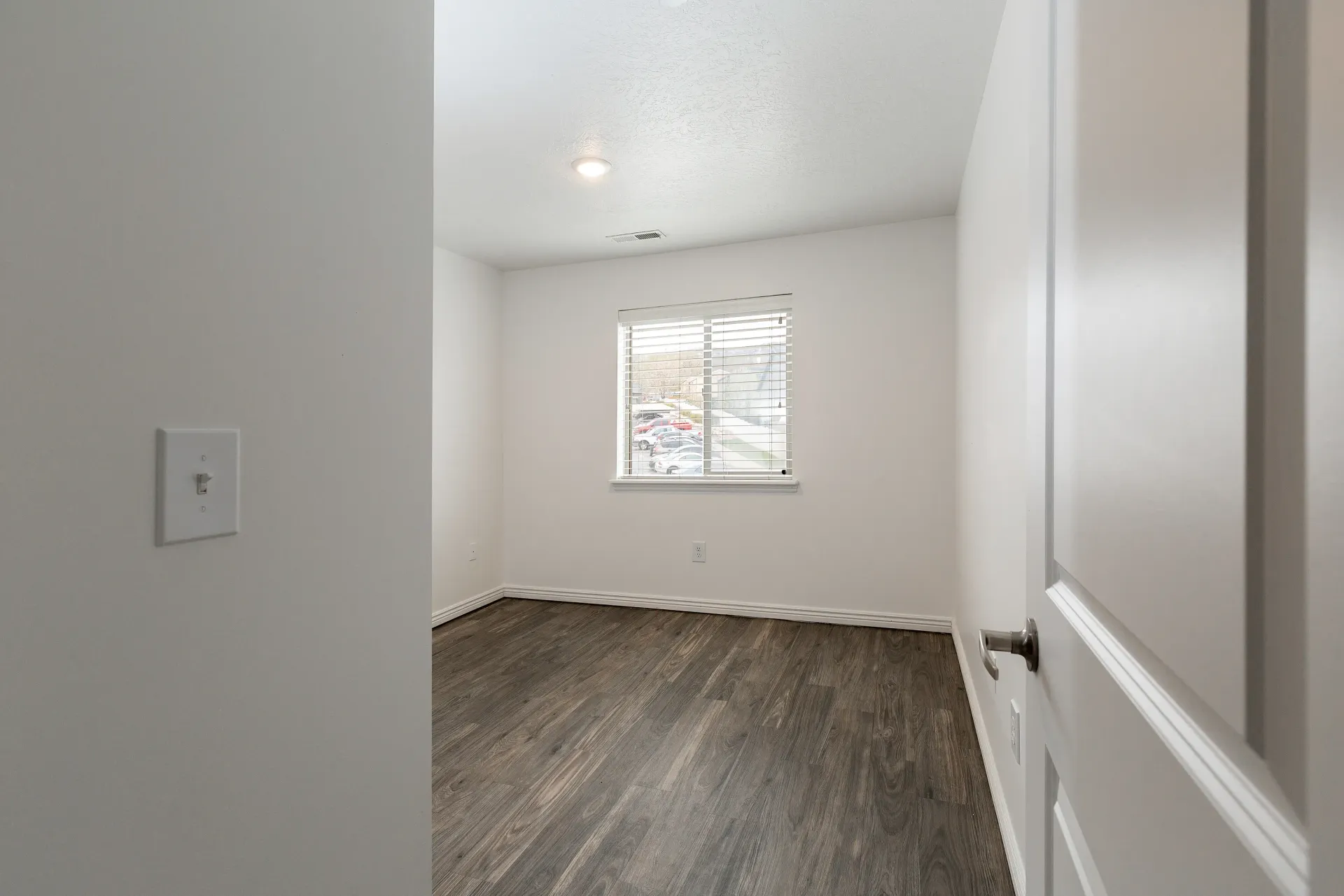 Empty bedroom with wood-look flooring and a window overlooking a parking lot.
