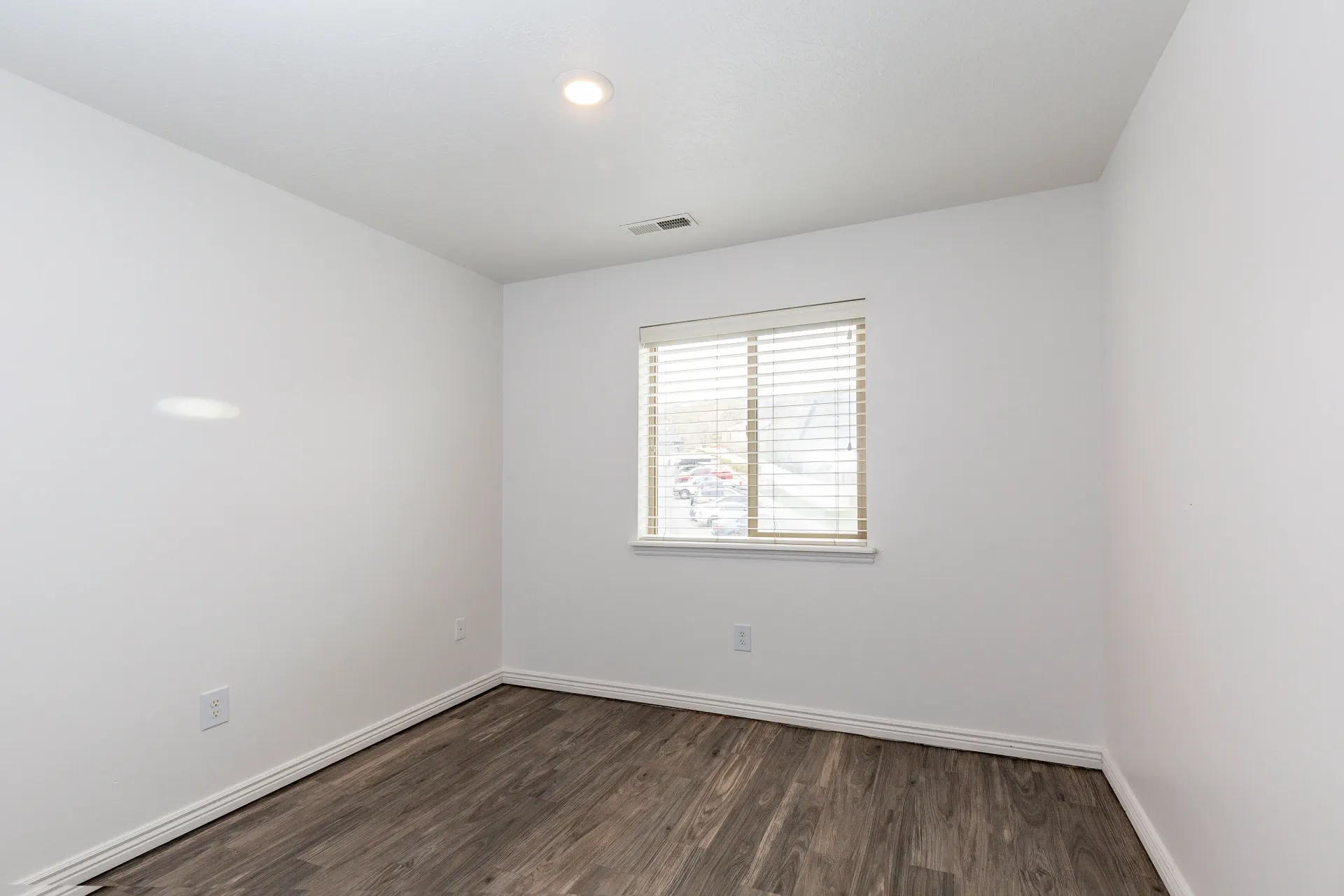 Empty bedroom with wood-look flooring and a window with blinds.