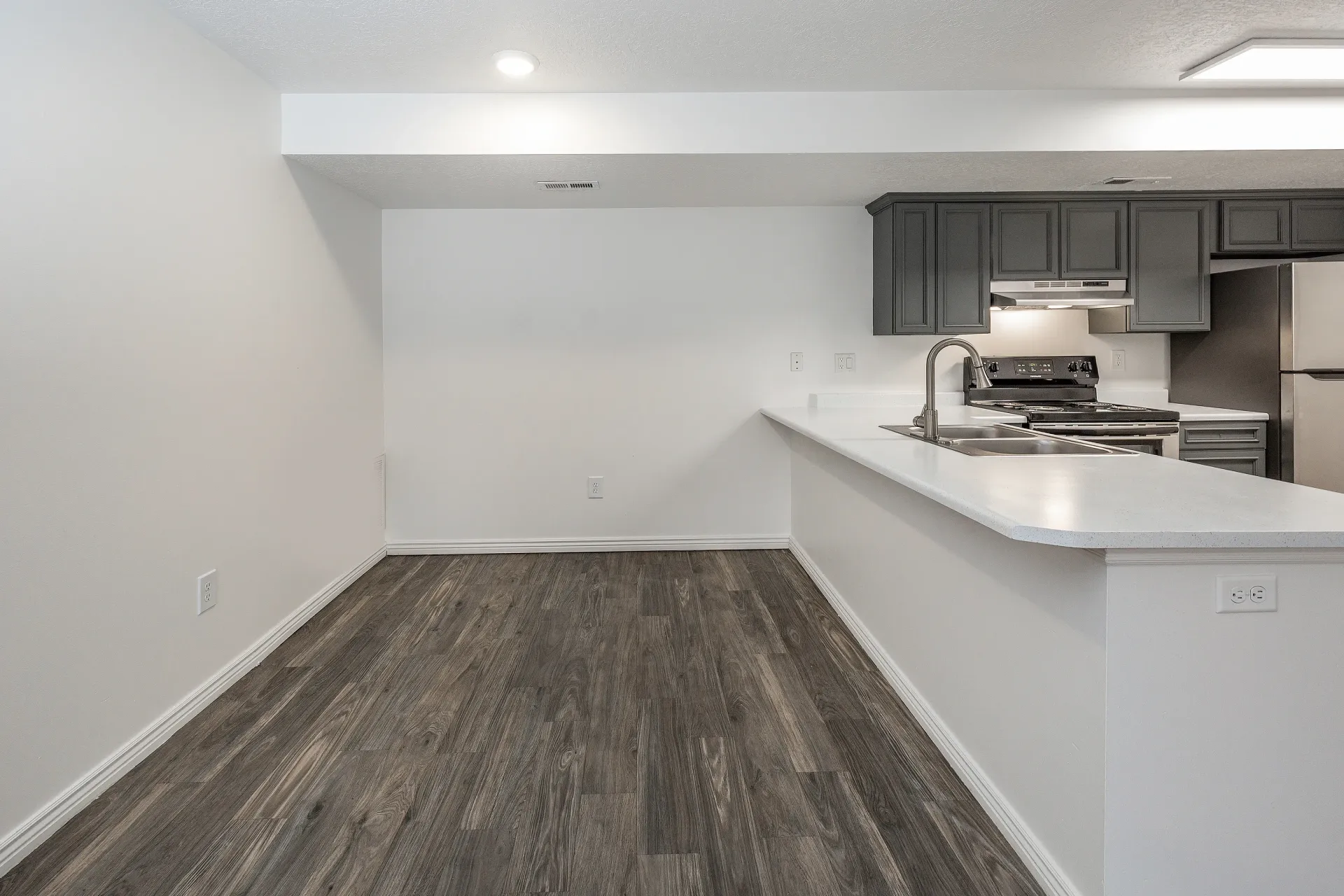 Modern kitchen with dark gray cabinets, white countertops, and stainless steel appliances.