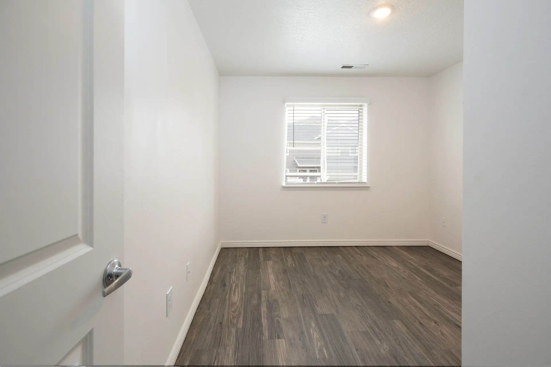 Empty room with wood-look flooring and a window with blinds.