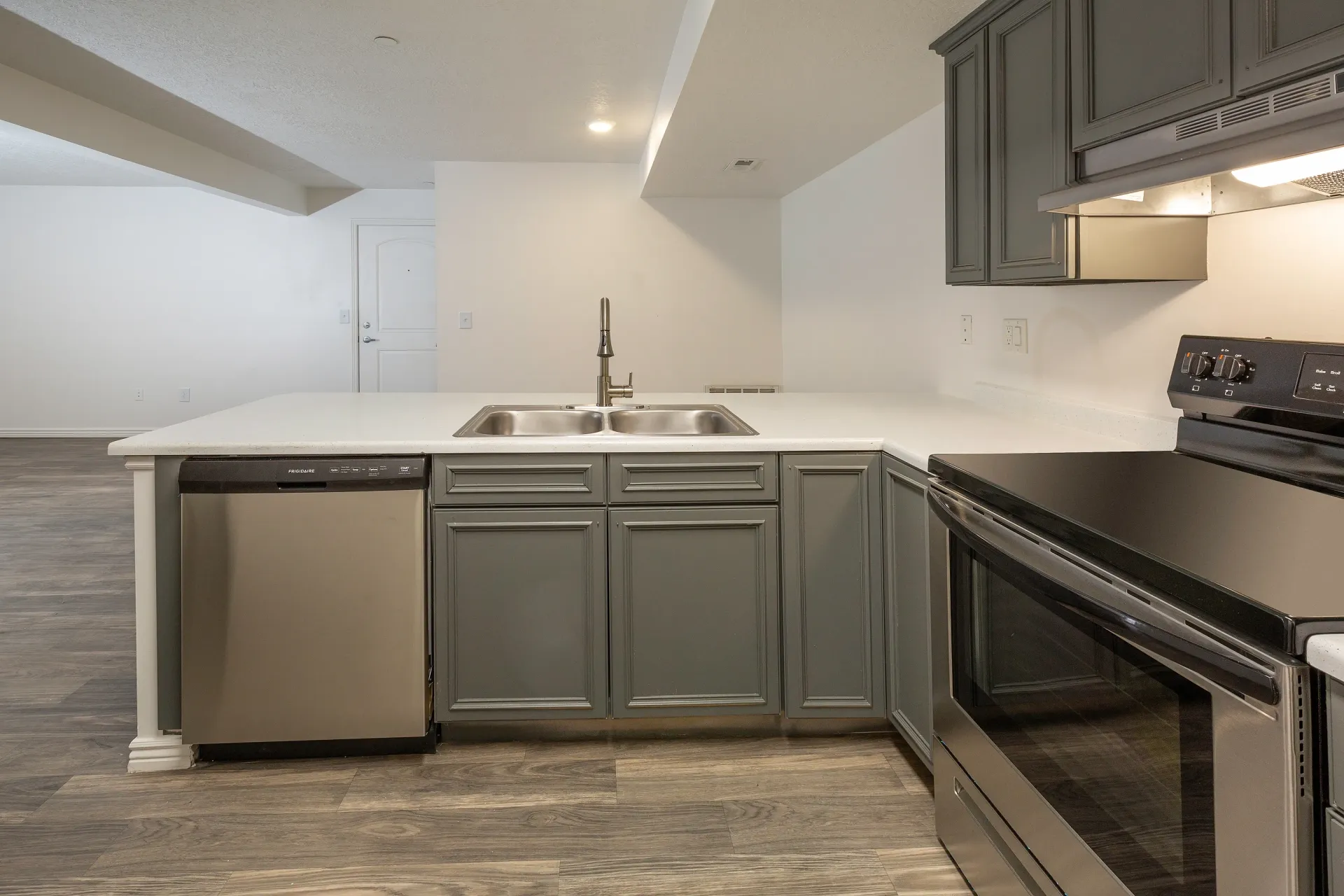 Kitchen with gray cabinets, stainless steel dishwasher, double sink, and black range.
