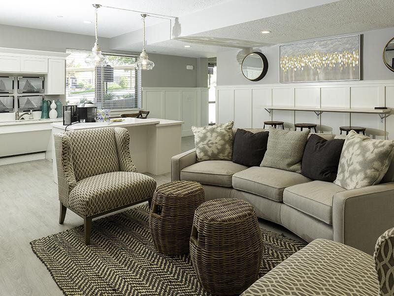 Bright modern living room with gray sofa, patterned chairs, woven ottomans, and open kitchen in the background
