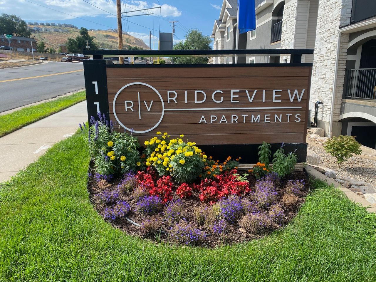 Ridgeview Apartments sign beside a sidewalk, bordered by colorful flower bed and green grass.