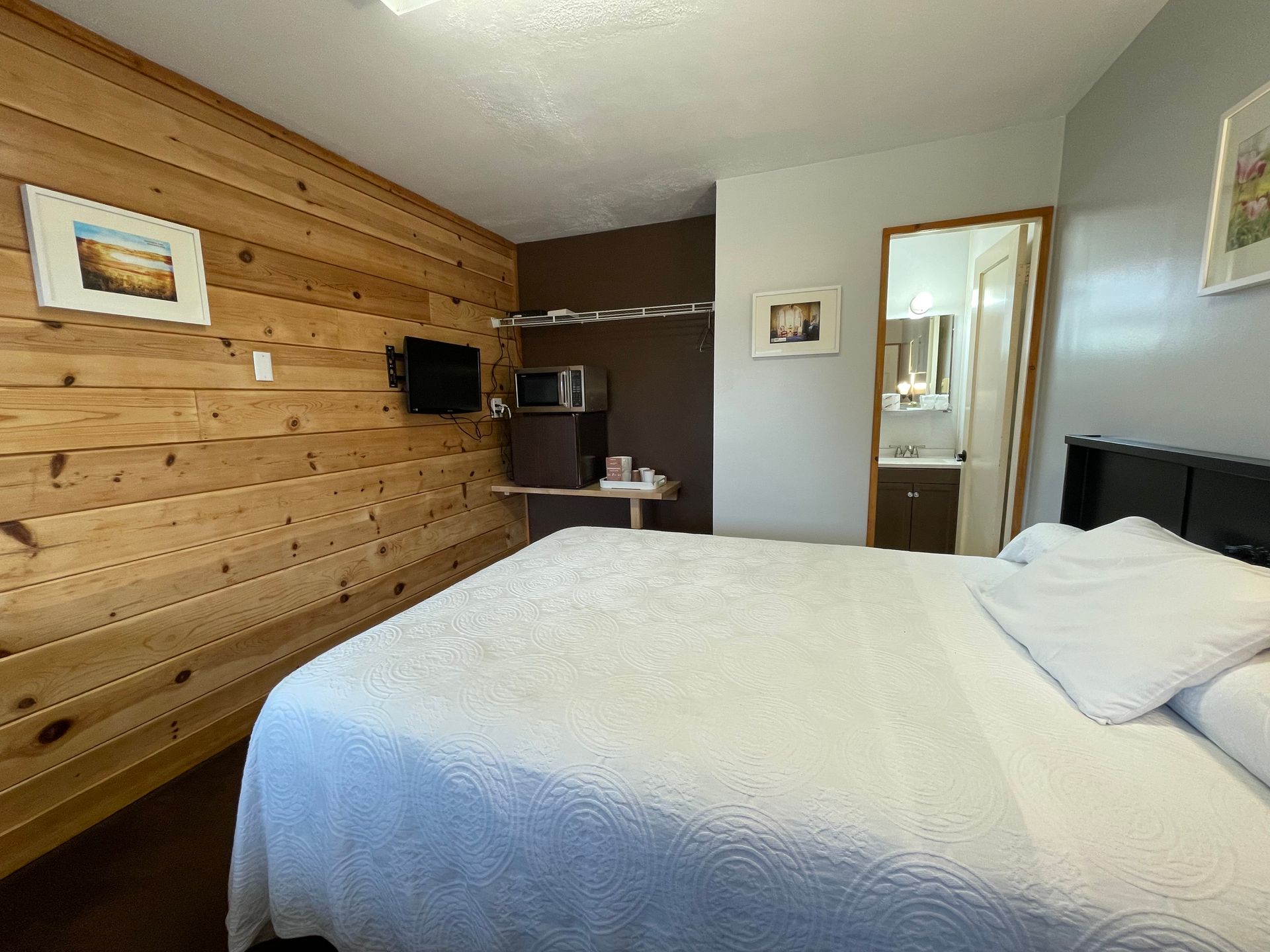 A bedroom with a king size bed , wooden walls , a microwave and a refrigerator.