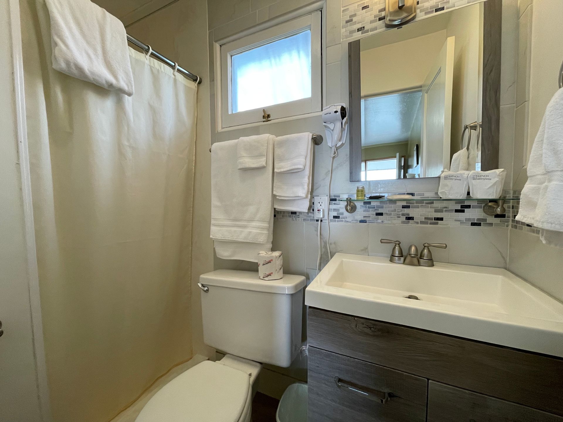 A bathroom with a toilet , sink , mirror and shower curtain.