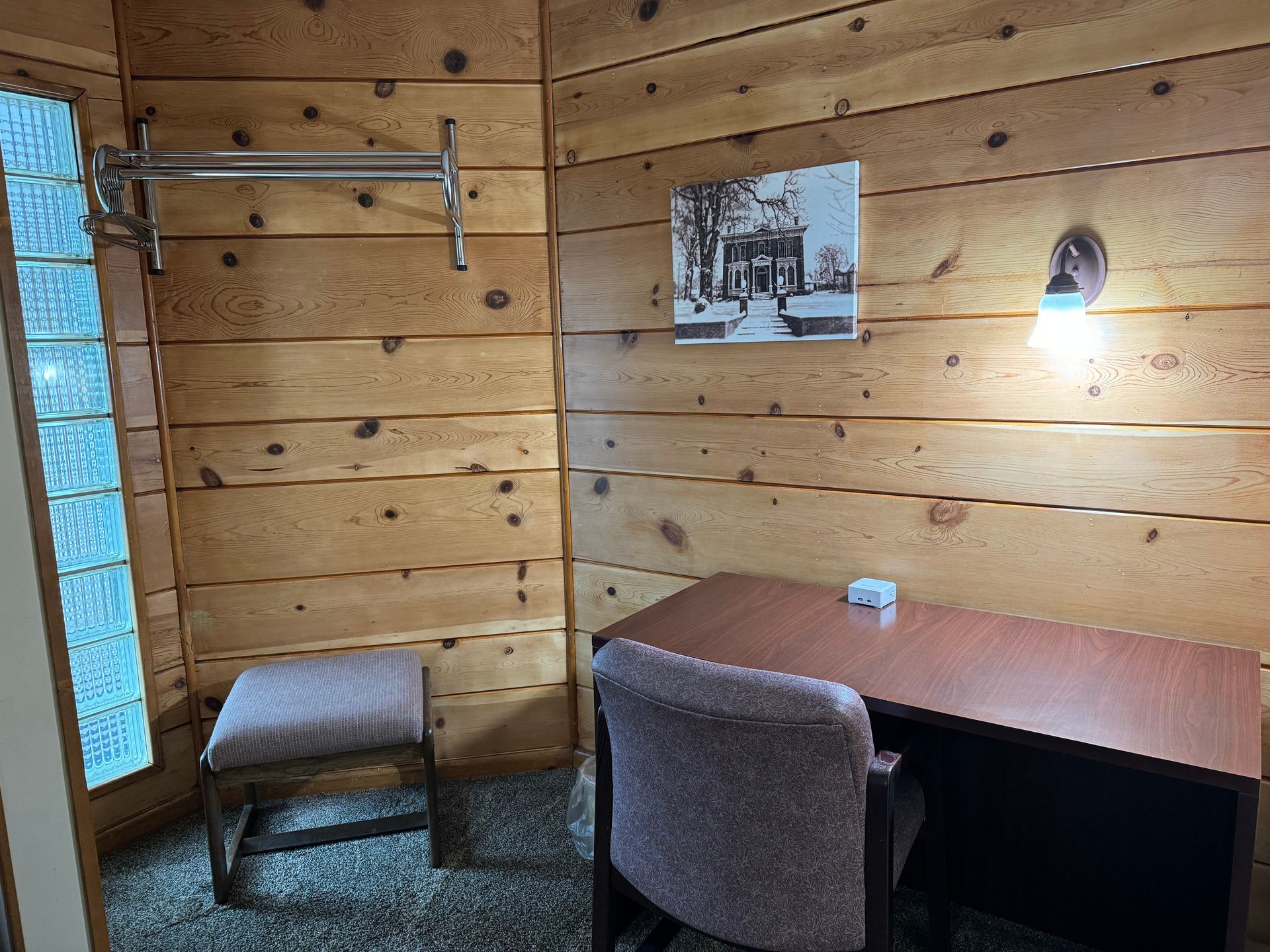 A wooden room with a desk and chair and a picture on the wall.